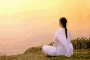 mujer de espaldas meditando hacía el sol amaneciendo